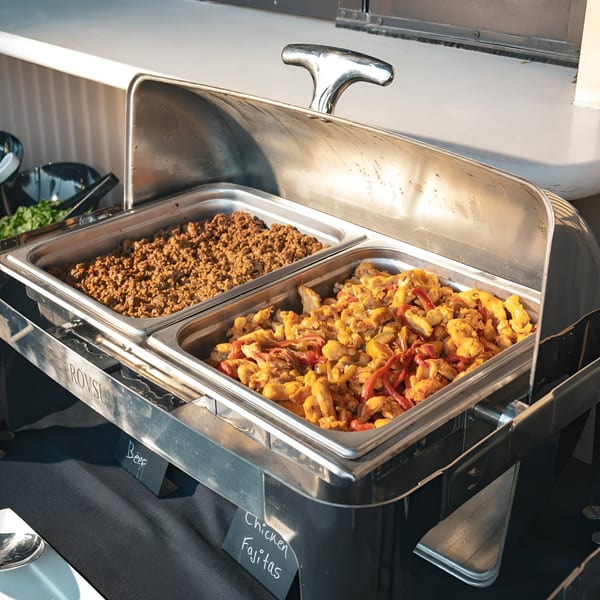 Chafing dishes filled with seasoned ground beef and chicken fajitas with peppers, ready for serving.