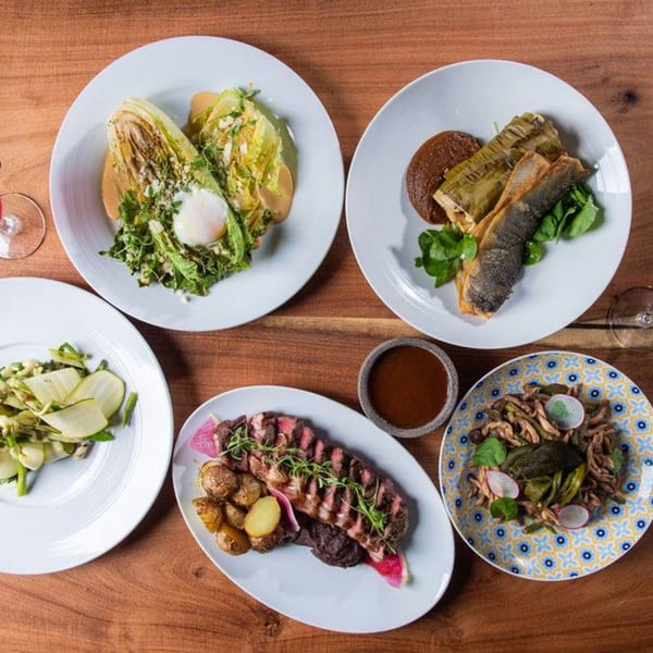 Overhead view of five Mexican dishes, including steak, fish, salad, and pasta, on a wooden table.