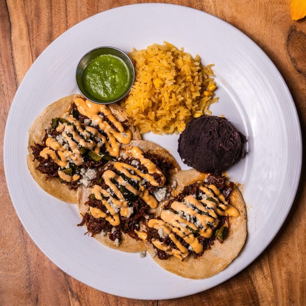 Three Ofrenda Mexican tacos with rice, black beans, and green salsa on a white plate.