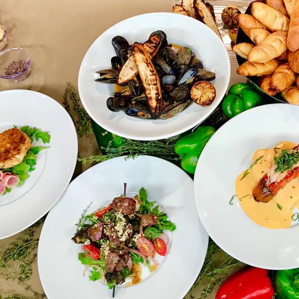 Four plates of Mexican cuisine, including mussels, skewers, and a lobster dish, with bread and peppers.