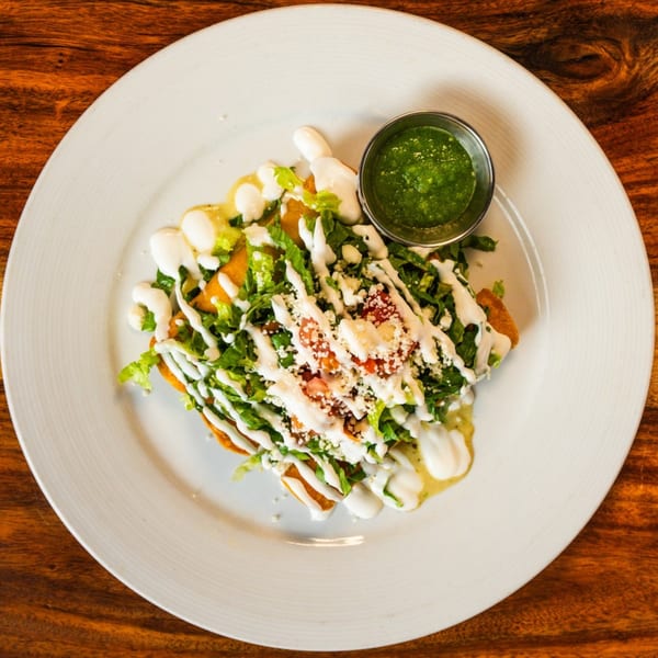 Ofrenda's Mexican flautas, topped with lettuce, cheese, crema, and a side of green salsa.