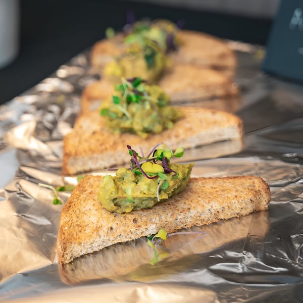 Toasted bread slices topped with guacamole and microgreens, arranged on aluminum foil.