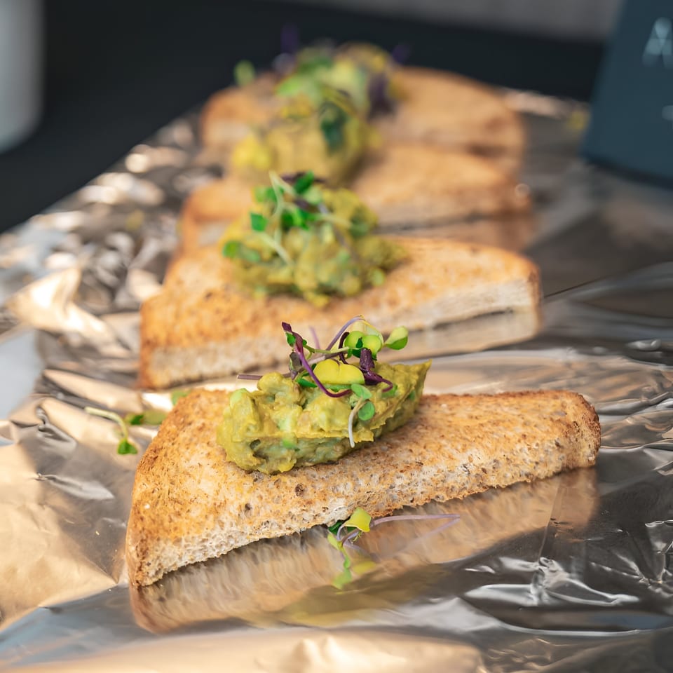 Toasted bread slices topped with guacamole and microgreens, arranged on aluminum foil.