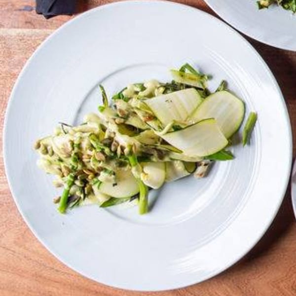 Ofrenda's Mexican zucchini salad with green beans, creamy dressing, and pumpkin seeds on a white plate.