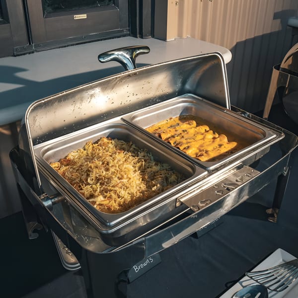 Chafing dish with Mexican food, including shredded potatoes and enchiladas in yellow sauce.