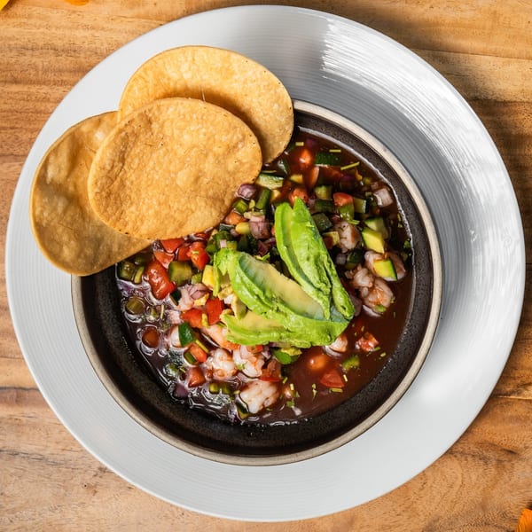 Ofrenda's shrimp ceviche with avocado, diced vegetables, and two tostadas on a white plate.
