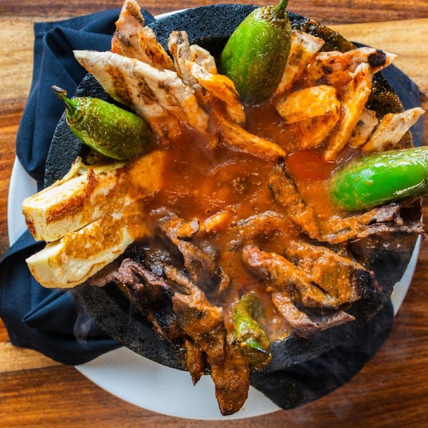 Steaming Ofrenda molcajete with grilled chicken, steak, cheese, and green peppers in a rich red sauce.