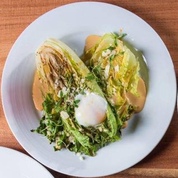 Ofrenda's grilled romaine salad with a poached egg, dressing, and crumbled cheese on a white plate.
